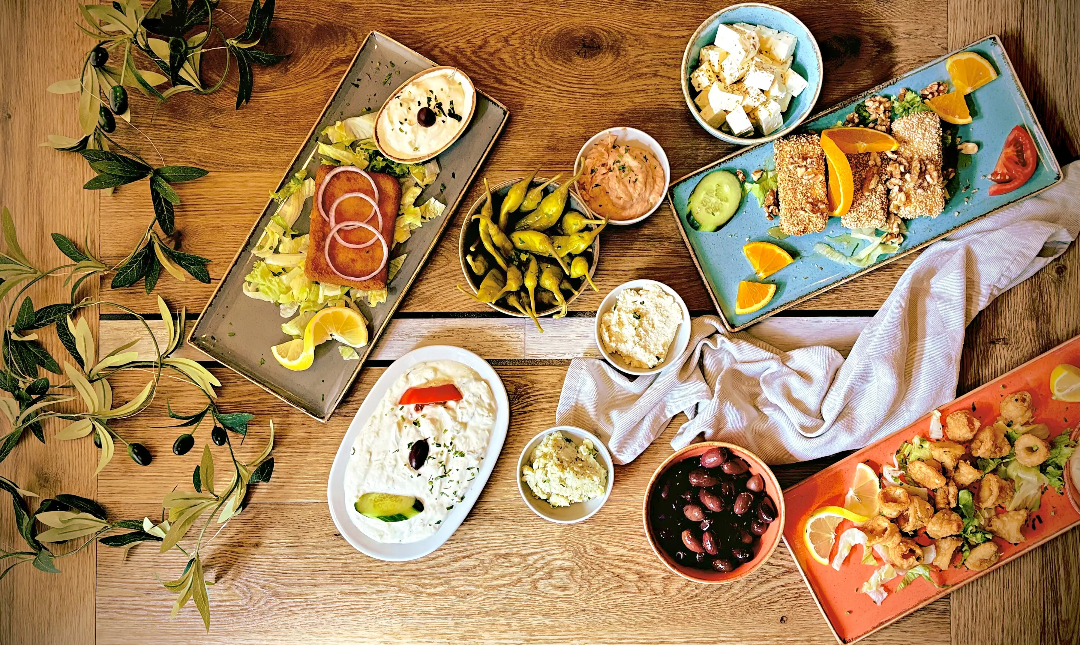 Griechische Vorspeisen auf einem Holztisch: Zaziki, Oliven, Feta, Dolmadakia und Sesam-Saganaki