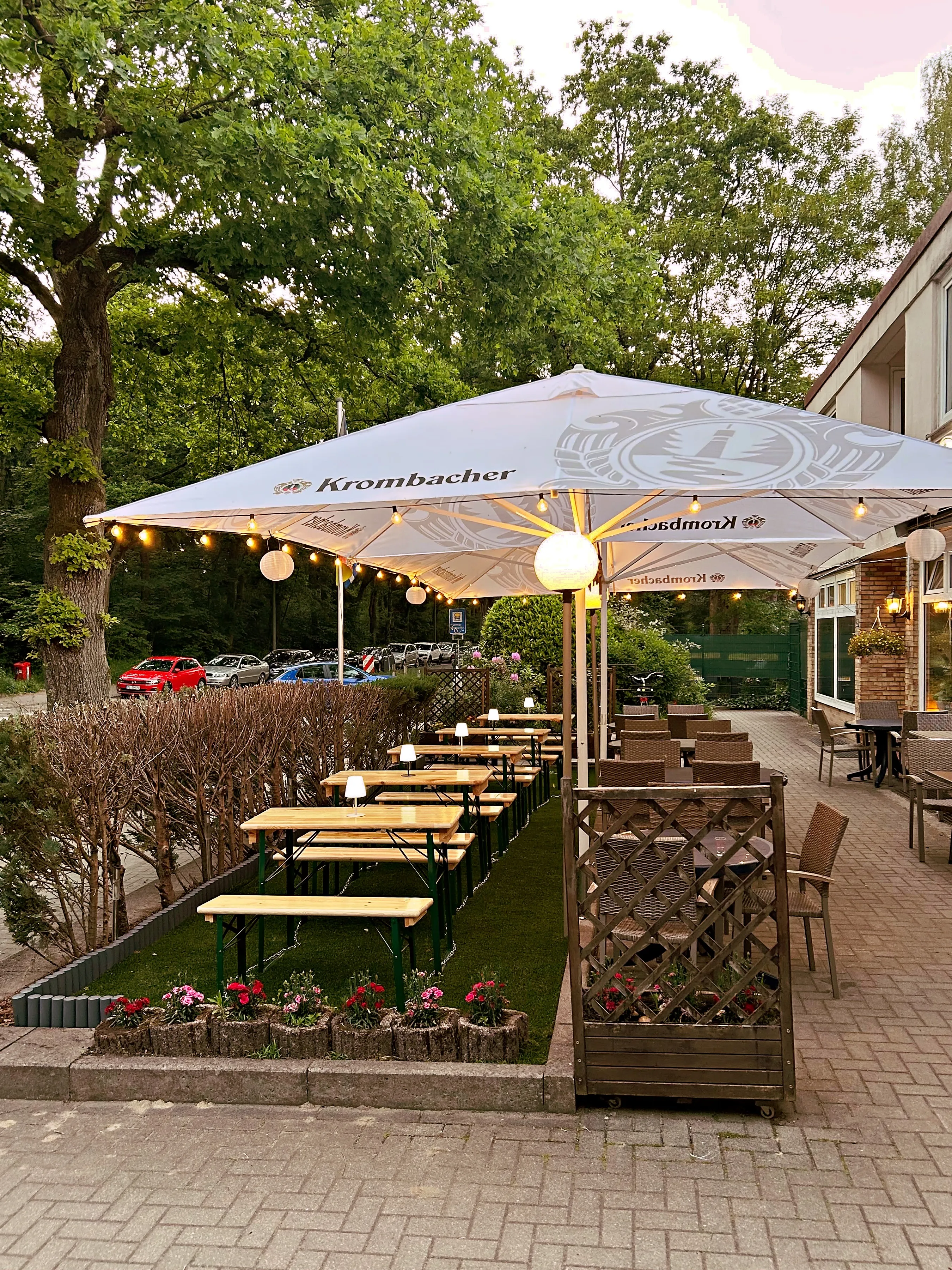 Die Terrasse mit Sonnenschirmen und Lichterketten unter alten Bäumen